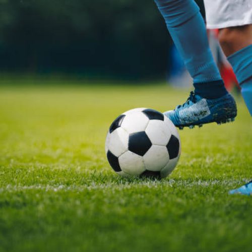 Close up of legs and feet of football player in blue socks and shoes running and dribbling with the ball. Soccer player running after the ball. Sports venue in the background