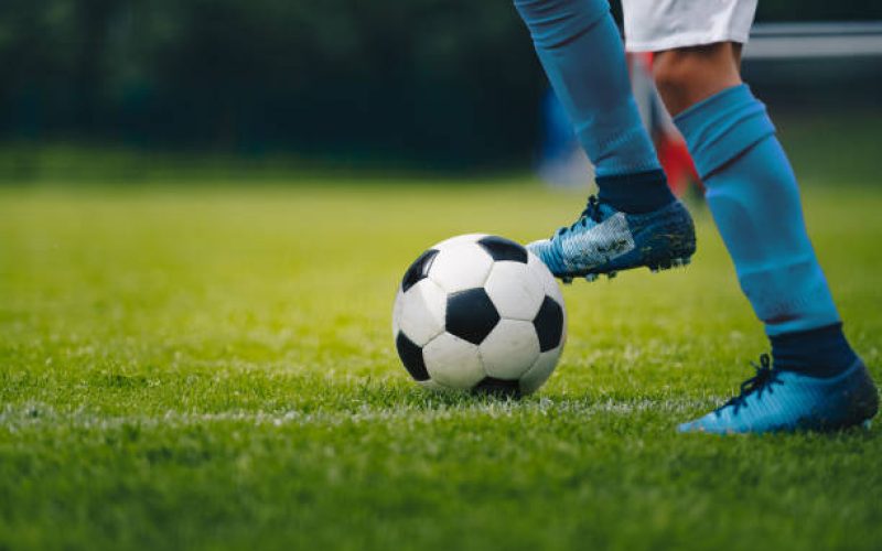 Close up of legs and feet of football player in blue socks and shoes running and dribbling with the ball. Soccer player running after the ball. Sports venue in the background