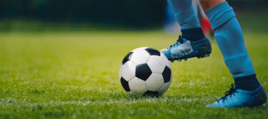 Close up of legs and feet of football player in blue socks and shoes running and dribbling with the ball. Soccer player running after the ball. Sports venue in the background